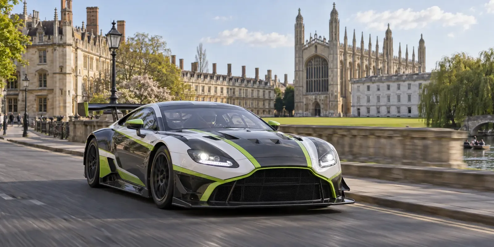 Race-liveried GT car travelling through Cambridge beside historic university architecture