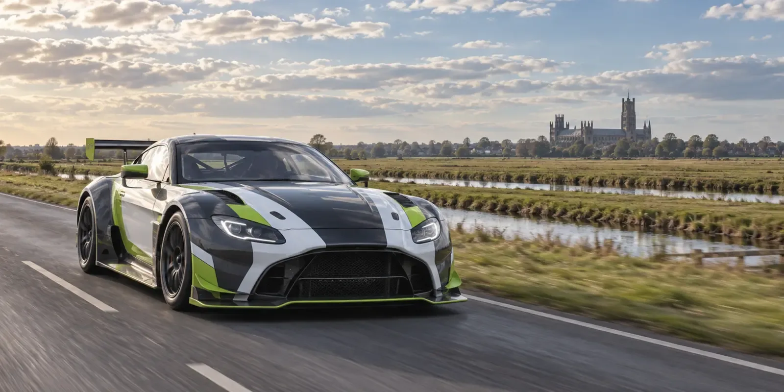 Race-liveried GT car travelling across the Cambridgeshire Fens with Ely Cathedral in the distance